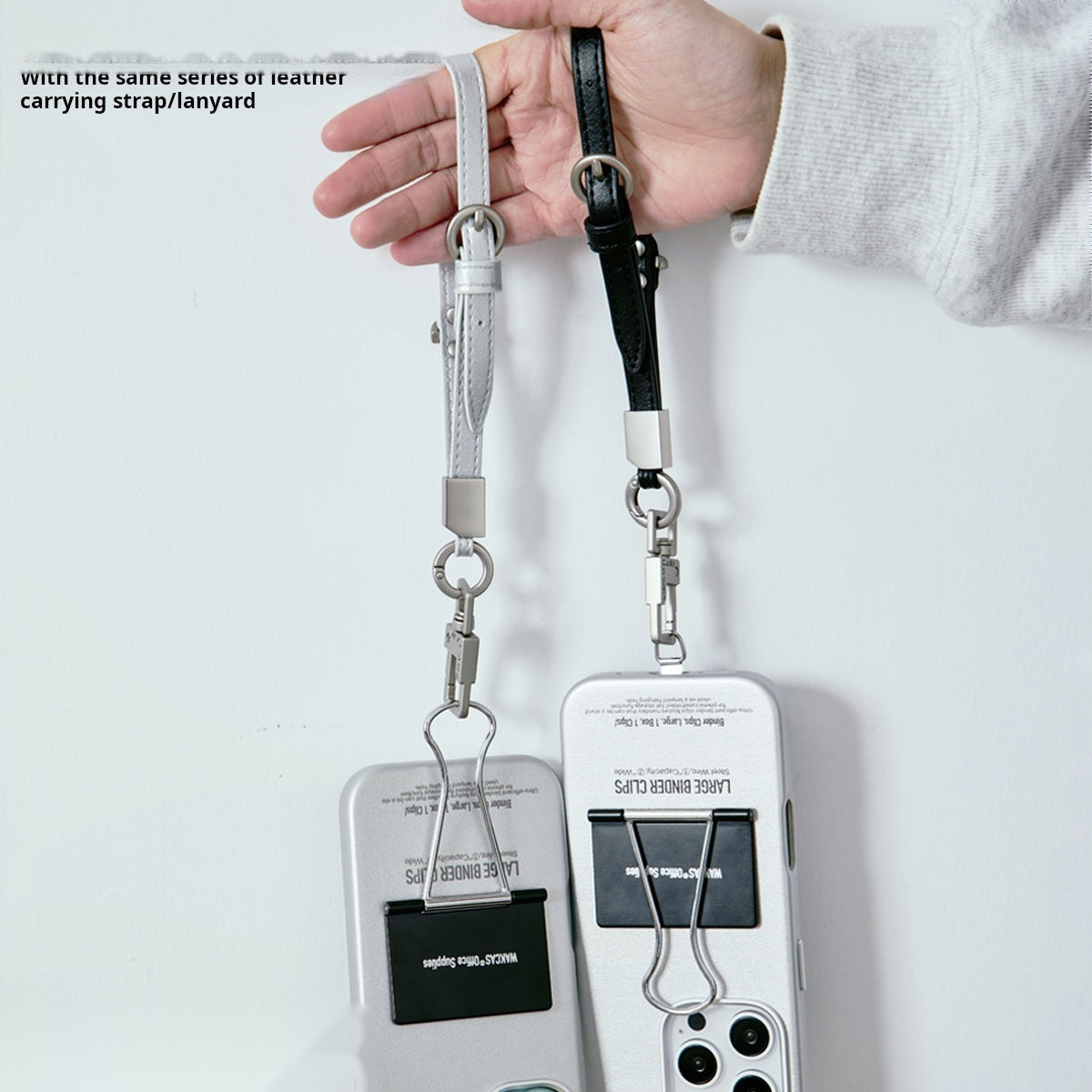 Hand holding two binder clip cases by their black and silver wrist straps
